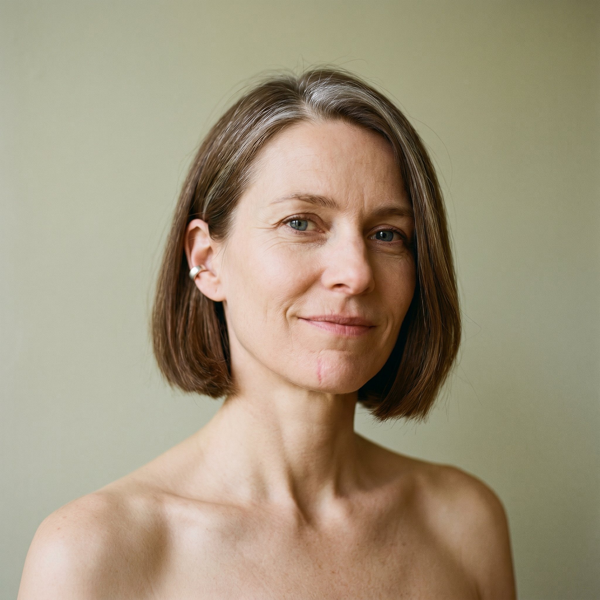 Establishing-Portrait Frame, 1:1 head-and-bare-shoulders Naked-Base, Henrike Brandt-Klausen frontal direct-gaze, void pale-olive Vorraum-wall background, soft directional window light camera-left, 100%-from-text Subject-Lock anchor for all subsequent frames
